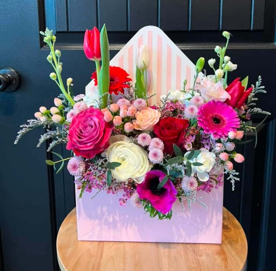Love Letter Flower Arrangement in a pink paper letter box with colorful blooms.